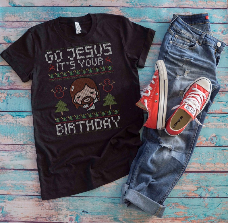 May include: Black t-shirt with the text "GO JESUS IT'S YOUR BIRTHDAY" in a pixelated design. The shirt features a cartoon Jesus, snowmen, and Christmas trees. Paired with blue jeans and red Converse sneakers.