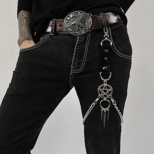 May include: A black leather belt with a silver eagle buckle and a silver chain with a pentagram charm attached to it.