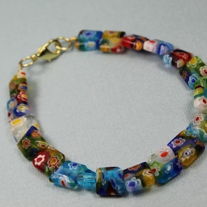 May include: A colorful glass bead bracelet with a gold clasp. The beads are square and feature a variety of floral patterns in shades of blue, green, red, yellow, and white.