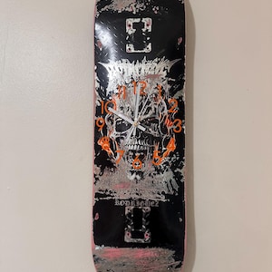 May include: Black skateboard with a skull clock design. The clock hands are silver, and the numbers are orange. The skateboard has a pink edge and the word "RODRIGUEZ" is printed on the board.