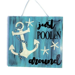 Puede incluir: Un letrero de madera azul con un ancla blanca y el texto "just poolen around" en negro. Tambi&eacute;n hay tres estrellas de mar blancas en el letrero.