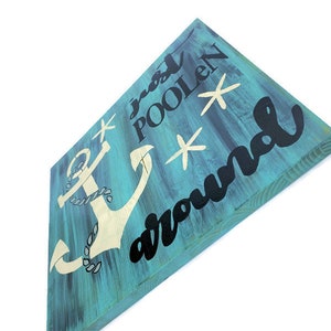 Puede incluir: Un letrero de madera azul turquesa con un ancla blanca y el texto "Just Poolen Around" en negro. El letrero tiene tres estrellas de mar blancas.