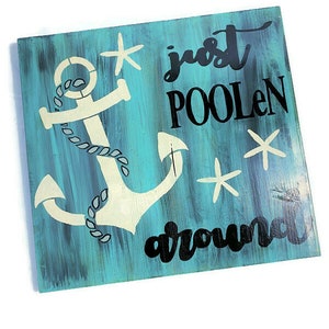 Puede incluir: Un letrero de madera azul turquesa con un ancla blanca y texto negro que dice "just poolen around". El letrero tiene un aspecto desgastado y presenta estrellas de mar blancas.