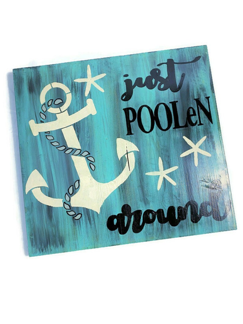 Puede incluir: Un letrero de madera azul turquesa con un ancla blanca y texto negro que dice "just poolen around". El letrero tiene un aspecto desgastado y presenta estrellas de mar blancas.