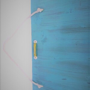 Puede incluir: Una puerta de madera azul claro con un tirador de cuerda blanca. La puerta est&aacute; cerrada y el tirador de cuerda est&aacute; atado en un nudo en la parte superior e inferior.