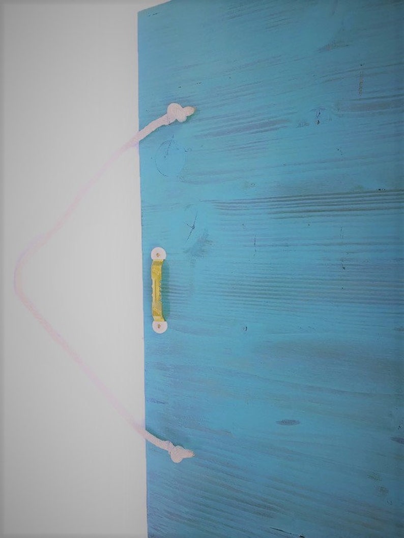 Puede incluir: Una puerta de madera azul claro con un tirador de cuerda blanca. La puerta est&aacute; cerrada y el tirador de cuerda est&aacute; atado en un nudo en la parte superior e inferior.