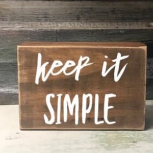 May include: A wooden sign with the text "keep it simple" painted in white on a brown background.