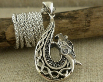 May include: A silver pendant in the shape of a dragon's head with black gemstones set in the design. The pendant is on a silver chain.