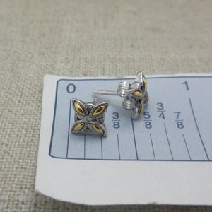 Peut inclure: Une paire de boucles d'oreilles &agrave; clous argent&eacute;es avec un motif de papillon dor&eacute;. Les boucles d'oreilles sont sur une r&egrave;gle blanche et bleue. Les boucles d'oreilles mesurent environ 1 cm.
