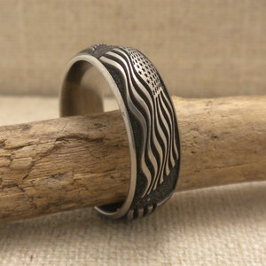 Op de afbeelding: Een zilveren ring met een gegraveerd Amerikaans vlagontwerp. De ring ligt op een houten oppervlak.