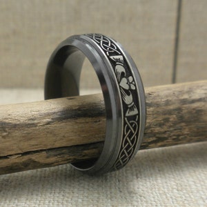 Op de afbeelding: Een zwarte en zilveren trouwring met een Keltisch knoopontwerp en een klavertjevier. De ring is gemaakt van wolframcarbide.