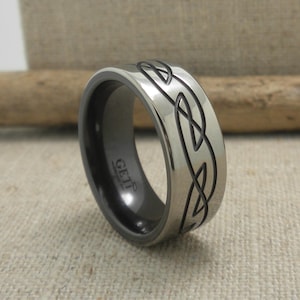 Op de afbeelding: Een zwarte en zilveren trouwring met een Keltisch knoopontwerp. De ring is gegraveerd met het woord "GETIT".