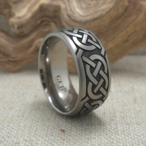 Op de afbeelding: Een zilveren titanium ring met een Keltisch knoopontwerp. De ring is aan de binnenkant gegraveerd met de woorden "GETP".