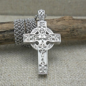 May include: A silver Celtic cross pendant with intricate knotwork designs. The cross is on a silver chain.