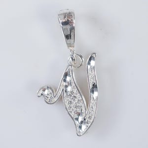 May include: A silver pendant in the shape of the letter V. The pendant has a textured, diamond-shaped pattern.