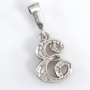 May include: A silver-toned metal pendant shaped as the cursive letter E. The surface of the letter features a textured, sparkling finish with polished, smooth edges. A small jump ring connects the letter to a tapered, polished silver-toned bail.