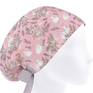 Op de afbeelding: Een roze scrubmuts met een bloemen- en konijnenprint. De muts heeft een grijze strik.