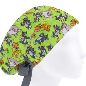 Peut inclure: Une coiffe de chirurgien vert citron avec un motif répété des personnages de dessins animés Tom et Jerry. La coiffe a une attache grise à l'arrière pour l'ajuster. Les personnages sont dans diverses poses, Tom et Jerry interagissant.