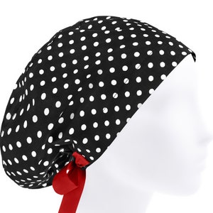 May include: A black scrub cap featuring a white polka dot pattern throughout the fabric. The cap has a rounded, gathered crown design and includes a bright red ribbon tie at the back, which is secured in a small bow with two hanging ends.