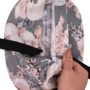 May include: A grey and pink floral scrub hat with a black elastic band. The hat is made of a soft, comfortable fabric and is designed to be worn by medical professionals.