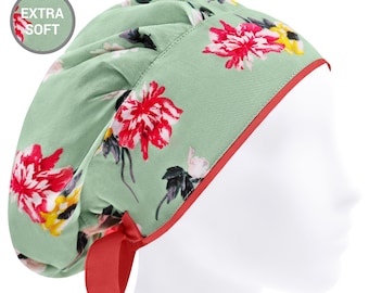 May include: A sage green scrub cap featuring a vibrant floral pattern with red and yellow flowers. The cap has a solid red trim along the bottom edge, a red tie closure at the back, and a circular badge in the upper left corner with the text EXTRA SOFT.