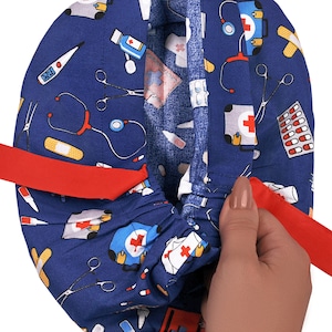 Peut inclure: Un bonnet de chirurgien bleu avec un lien rouge et divers motifs sur le th&egrave;me m&eacute;dical, notamment des st&eacute;thoscopes, des bandages, des pilules et des trousses de premiers soins.