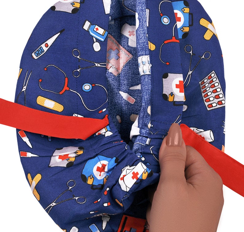 Peut inclure: Un bonnet de chirurgien bleu avec un lien rouge et divers motifs sur le th&egrave;me m&eacute;dical, notamment des st&eacute;thoscopes, des bandages, des pilules et des trousses de premiers soins.
