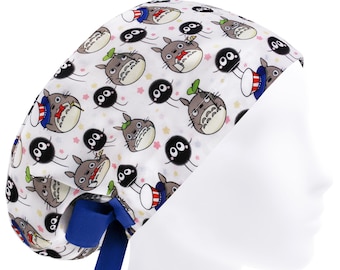May include: White scrub cap featuring a repeating pattern of cartoon characters and stars. The cap has a blue tie and is designed to fit comfortably. The characters are in shades of gray, black, and green.