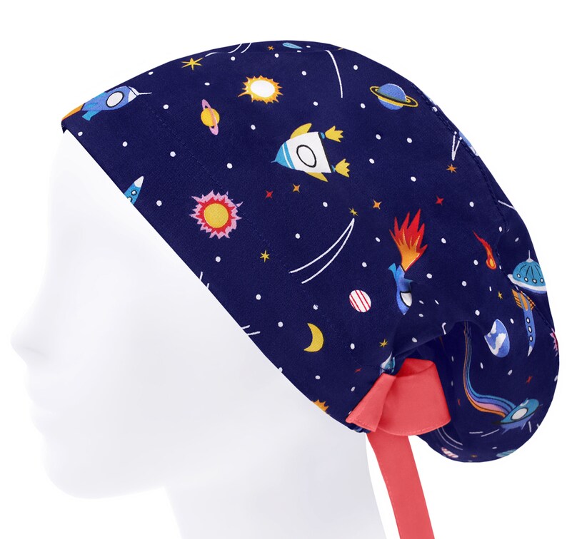 K&ouml;nnte beinhalten: Eine dunkelblaue OP-Haube mit einem bunten Weltraum-Muster aus Raketen, Planeten, Sternen und Kometen. Die Haube verf&uuml;gt &uuml;ber ein einfarbiges, korallenrotes Band am Hinterkopf, mit dem die Passform individuell angepasst werden kann.