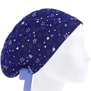 May include: A blue scrub hat with a white tie. The hat has a pattern of white stars and blue hearts on a dark blue background.