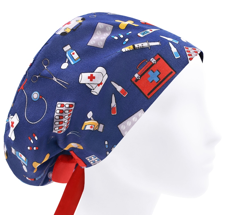 Peut inclure: Un bonnet de chirurgien bleu avec un lien rouge. Le bonnet est imprim&eacute; d'un motif de symboles et d'accessoires m&eacute;dicaux, notamment des pilules, des bandages, un st&eacute;thoscope et une trousse de premiers soins.