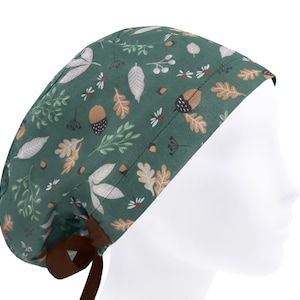 Pode incluir: Uma touca cirúrgica verde com um padrão de outono. A touca apresenta um design repetido de folhas, bolotas e pequenas flores em tons de branco, bege e castanho. Uma fita castanha está amarrada na parte de trás.