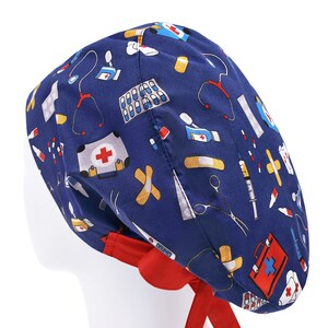 Peut inclure: Un bonnet de chirurgien bleu avec une cravate rouge. Le bonnet est orn&eacute; d'un motif de symboles et d'accessoires m&eacute;dicaux, notamment des bandages, des pilules, un st&eacute;thoscope et une trousse de premiers soins.