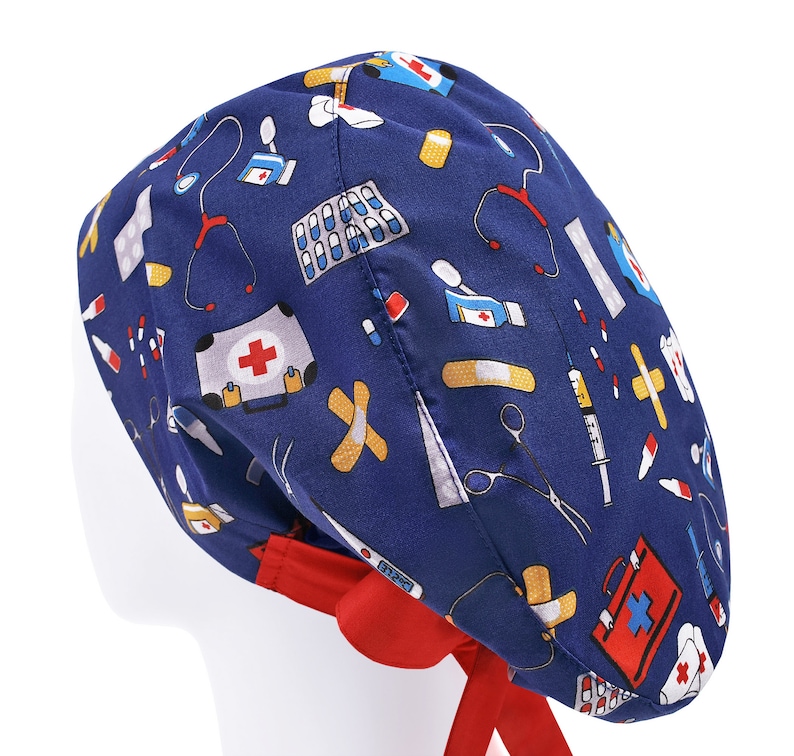 Peut inclure: Un bonnet de chirurgien bleu avec une cravate rouge. Le bonnet est orn&eacute; d'un motif de symboles et d'accessoires m&eacute;dicaux, notamment des bandages, des pilules, un st&eacute;thoscope et une trousse de premiers soins.