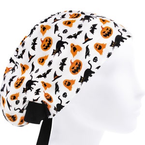 Puede incluir:  gorro de quirófano blanco con un estampado de temática de Halloween con calabazas naranjas, gatos negros, murciélagos, fantasmas y calaveras.