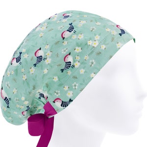May include: A light green scrub cap with a floral pattern featuring small white flowers and colorful birds. The cap has a pink tie.