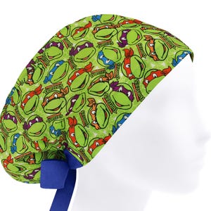 May include: A green scrub cap featuring a repeating pattern of Teenage Mutant Ninja Turtles faces in red, orange, purple, and blue. The cap has a blue band and ties.