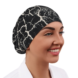 May include: A black and white patterned scrub cap with a cracked or marbled design. The cap is made of a soft, comfortable fabric and is designed to be worn by medical professionals.