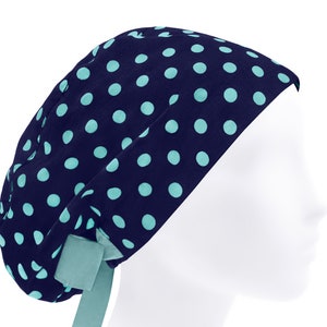 May include: A navy blue scrub cap featuring a repeating pattern of light turquoise polka dots. The cap has a rounded crown and includes a matching light turquoise fabric tie at the back to secure the fit, shown on a white mannequin head.