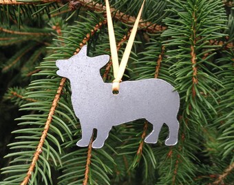 May include: A silver metal ornament shaped like a dog, hanging from a yellow ribbon on a green pine tree branch.