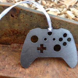 May include: A metal ornament shaped like a video game controller. The ornament is gray and has a white ribbon attached to it.