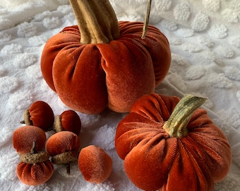 May include: A set of velvet pumpkins in shades of orange. The pumpkins are decorated with a stem and have a textured surface. There are also several smaller velvet pumpkins in the image.