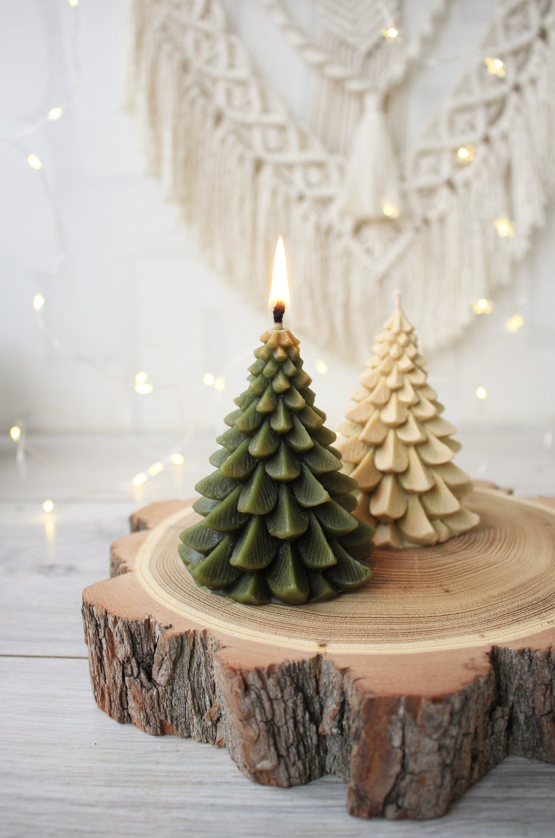 May include: Two green and beige Christmas tree shaped candles on a wooden slice. The green candle is lit.