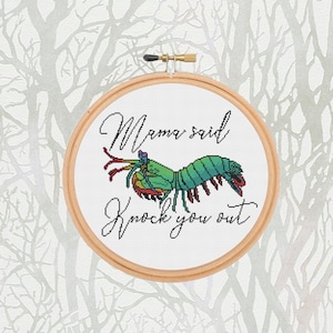 May include: A white embroidery hoop with a green and red mantis shrimp design and the text "Mama said knock you out".
