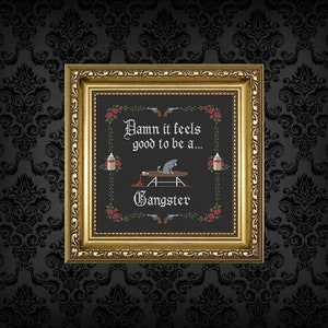 Peut inclure: Une broderie au point de croix encadrée avec le texte "Damn it feels good to be a... Gangster." Le motif comprend des armes à feu, des roses et un chat. Le cadre est doré, et le fond est un papier peint sombre à motifs.