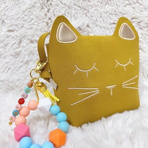 May include: A yellow cat-shaped purse with a gold chain and a colourful silicone beaded bracelet with the word "HALLO" spelled out.