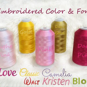 Pode incluir: Cinco carret&eacute;is de fio para bordar em diferentes cores: rosa claro, dourado, dourado escuro, rosa e rosa escuro. Os carret&eacute;is s&atilde;o etiquetados com os nomes das cores. O texto "Embroidered Color & Font" est&aacute; na parte superior da imagem. O texto "Love Classic Camelia WALT Kristen Block" est&aacute; na parte inferior da imagem.