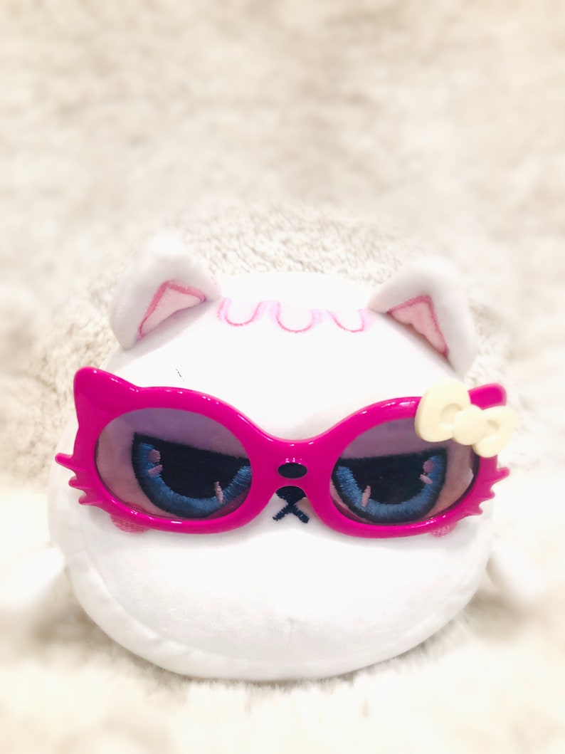 May include: White plush toy with pink ears and a pink bow. The toy is wearing pink sunglasses with a blue and white design.