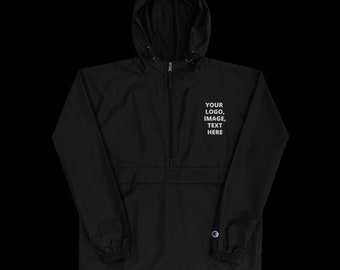 May include: Black hooded anorak jacket with a half-zip closure and a front pocket. The jacket features the text "YOUR LOGO, IMAGE, TEXT HERE" in white. The Champion logo is visible on the lower right side.