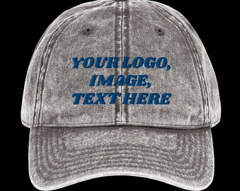 Op de afbeelding: Een grijze, verweerde denim baseballpet met blauwe geborduurde tekst die "YOUR LOGO, IMAGE, TEXT HERE" luidt.
